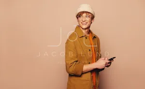 Cheerful young man using smartphone against vibrant peach background